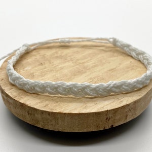 May include: A white braided bracelet on a wooden surface.