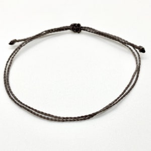 May include: A simple brown string bracelet with a knotted closure.