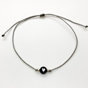 May include: A gray string bracelet with a black bead featuring a white heart design.