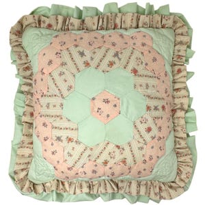 May include: A square throw pillow featuring a central patchwork design of alternating mint green and floral-patterned fabric hexagons. The pillow is bordered by a double-layered ruffled edge in matching mint green and beige floral fabric.