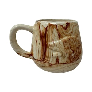 May include: A ceramic mug with a rounded body and a curved handle, featuring a marbled pattern of swirling cream and reddish-brown colors. The surface has a glossy finish with visible texture and a slightly uneven rim, creating a distinct appearance.