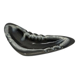 May include: A boomerang-shaped ceramic ashtray featuring a glossy finish with a dark charcoal gray base color and a white, mottled glaze along the raised edges. The piece has a smooth, curved silhouette with integrated notches for resting items.