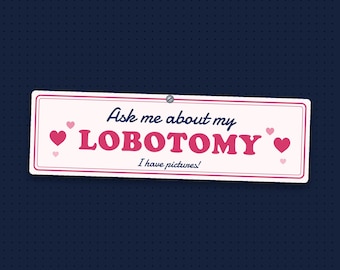 May include: A rectangular white sign with a pink border featuring the dark blue text Ask me about my LOBOTOMY and the smaller text I have pictures! in dark blue. The design includes several small pink hearts scattered around the text.