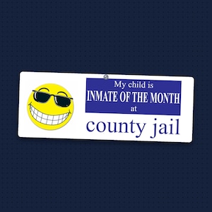 May include: A rectangular white bumper sticker featuring a yellow smiley face wearing black sunglasses on the left. The text reads: My child is INMATE OF THE MONTH at county jail. The text is printed in blue, with the middle section on a blue block.