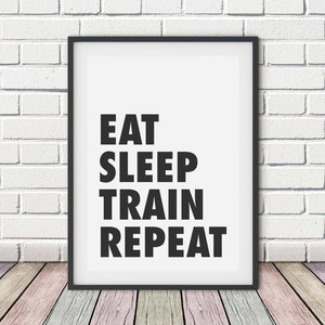 Könnte beinhalten: Schwarz-weißes Motivationsposter mit dem Text "Eat Sleep Train Repeat" in einem schwarzen Rahmen vor einer weißen Backsteinwand.