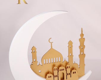 May include: A white crescent moon sculpture with a gold mosque cutout inside. The mosque has a dome and minarets. The sculpture is on a white base.