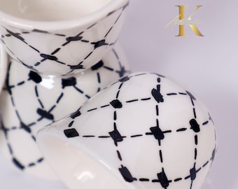 May include: A set of four white ceramic egg cups with a black and white geometric pattern. The cups are stacked on top of each other.