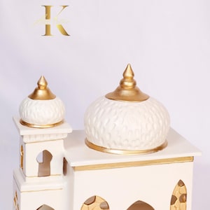 Può includere: Moschea in ceramica bianca con accenti dorati. La moschea ha due cupole, una più grande dell'altra, e dettagli intricati sulle pareti.