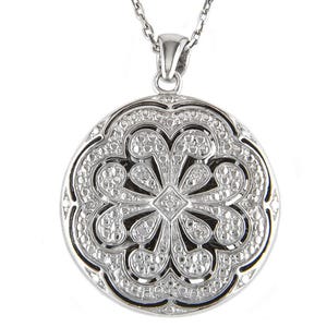 May include: A silver-toned pendant necklace featuring a round, openwork design. The pendant has a floral pattern with small, sparkling accents. The necklace chain is also silver-toned, creating a cohesive and elegant look.