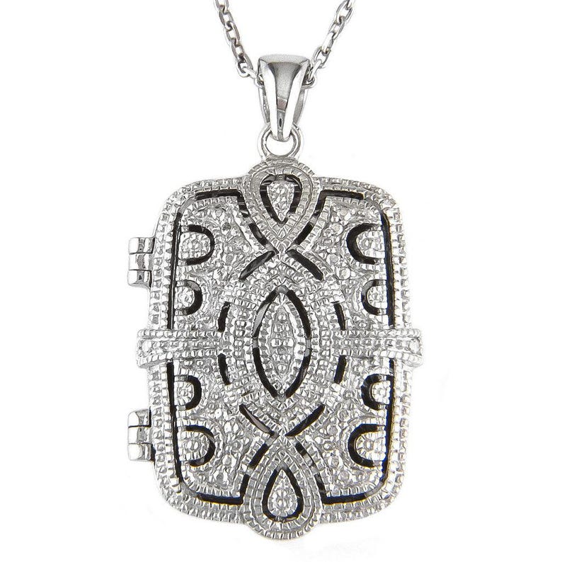 May include: A silver-colored rectangular locket pendant with an intricate filigree design. The pendant hangs from a delicate chain. The locket has a hinged opening and a detailed, textured surface.