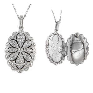 May include: A silver-toned locket necklace with a floral design. The pendant is oval-shaped and opens to reveal a compartment. The front of the pendant is encrusted with small, sparkling stones. The necklace chain is also silver.