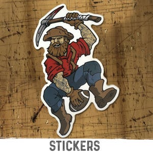 May include: A die-cut sticker featuring a bearded prospector wearing a brown hat, red shirt, and blue pants. The character holds a pickaxe above their head with one hand and a brown football in the other, with visible arm tattoos on both arms.