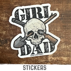 May include: A black and white sticker with a skull and crossbones design. The skull is surrounded by the words "Girl Dad" and the text "@kennyfarmerart" is at the bottom.