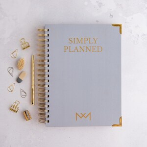 May include: A gray planner with gold accents and the text "SIMPLY PLANNED" and a gold monogram "M&M".