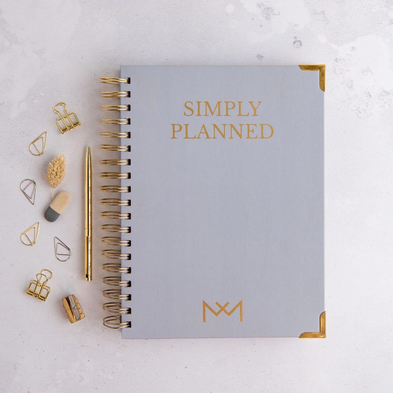 May include: A gray planner with gold accents and the text "SIMPLY PLANNED" and a gold monogram "M&M".