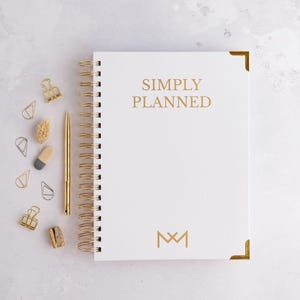 May include: White spiral bound planner with gold accents and the text "SIMPLY PLANNED" in gold lettering. The planner has a gold monogram of the letters "M" and "M" on the front cover.