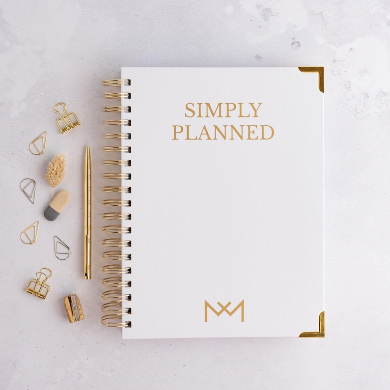 May include: White spiral bound planner with gold accents and the text "SIMPLY PLANNED" in gold lettering. The planner has a gold monogram of the letters "M" and "M" on the front cover.