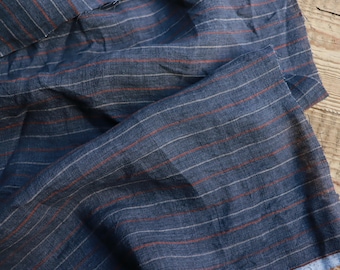 Puede incluir: Primer plano de una tela a rayas azules y rojas. La tela está tejida con finas rayas blancas y rayas rojas más gruesas. La tela está doblada y arrugada.