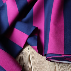 Peut inclure: Gros plan sur un tissu à rayures verticales audacieuses bleu marine et magenta. Le tissu est plié, révélant la texture et le motif. Le tissu est posé sur une surface en bois.