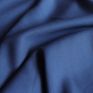 May include: Close-up of a navy blue fabric with soft folds and subtle texture. The material appears to be smooth and drapes naturally, creating shadows and highlights across its surface. The fabric's color is a deep, solid blue.