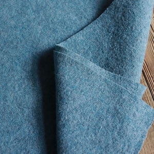 Puede incluir: Primer plano de un trozo de tela de fieltro azul doblado. La tela tiene una textura suave y peluda y es perfecta para proyectos de manualidades.