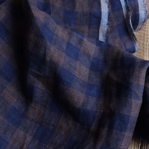 Puede incluir: Primer plano de una tela a cuadros azul oscuro y marrón. La tela está drapeada, mostrando su textura y patrón. El material parece ser lino o un textil ligero similar, adecuado para ropa o proyectos de decoración del hogar.