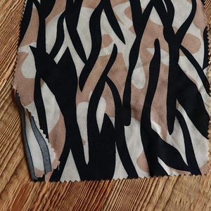 Pode incluir: Close-up de um tecido com um padrão abstrato preto e bege. O tecido tem uma textura macia e fluida.