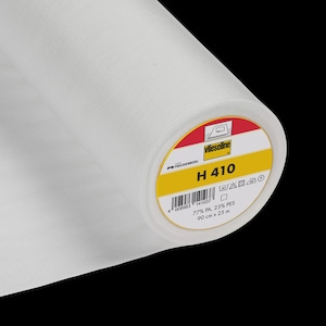 Peut inclure: Un rouleau de tissu d'entoilage blanc Vlieseline H 410. L'étiquette indique la marque Freudenberg, le nom du produit et les dimensions : 90 cm x 25 m. Le tissu est composé de 77 % de PA et de 23 % de PES.