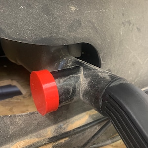May include: A close-up of a black vacuum cleaner hose with a red dust cap. The hose is connected to a black vacuum cleaner.