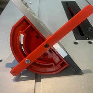May include: A red and silver table saw miter gauge with a protractor and a lever. The gauge is attached to a silver track.