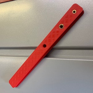 May include: A red plastic ruler with three brass screw holes. The ruler is about 12 inches long.