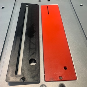 May include: Two table saw inserts, one black and one red, with a slot in the middle and a hole on the bottom. The inserts are made of plastic and have a textured surface.