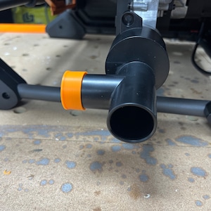 May include: Close-up of a black plastic pipe with an orange plastic cap. The pipe has a round opening at the end.