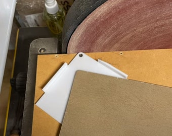 May include: A close-up of a sanding machine with a brown sanding disc. A white plastic sanding guide is placed on top of a brown piece of wood.