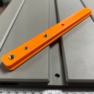 May include: Orange plastic bar with five brass threaded inserts. The bar is approximately 15 cm long.