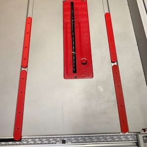 May include: A close-up of a table saw with a red blade guard and a ruler along the edge. The ruler is marked in inches and shows measurements from 0 to 650.