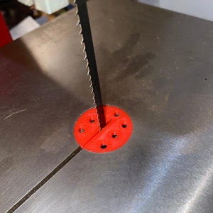 May include: A close-up of a red plastic blade guide for a band saw. The guide has multiple holes for adjusting the blade height.