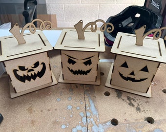 Könnte beinhalten: Drei hölzerne Kürbis-förmige Boxen mit Jack-o'-Lantern-Gesichtern. Die Boxen sind aus hellem braunem Holz gefertigt und haben ein schlichtes Design. Jede Box hat einen kleinen, geschnitzten Stiel oben.