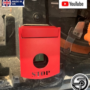 May include: A red safety switch with a green button and the word "STOP" in white lettering. The switch is mounted on a black machine.