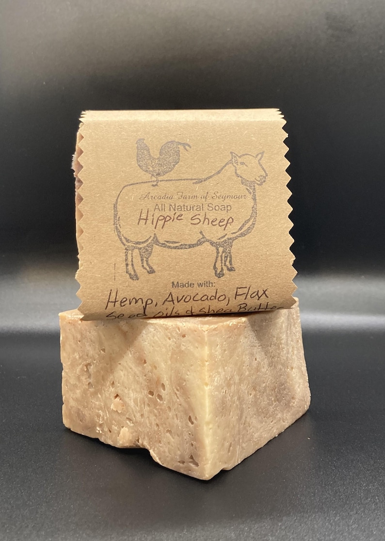 Może przedstawiać: Naturalne mydło w kostce z brązową papierową etykietą, na kt&oacute;rej widnieje napis "Arcadia Farm of Seymour Naturalne Mydło Hippie Sheep Wykonane z: Konopi, Awokado, Lnu Oleje z nasion i masło shea".