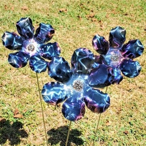 May include: Three metal flowers with blue and purple iridescent paint. The flowers are on thin metal stems and are arranged in a cluster.