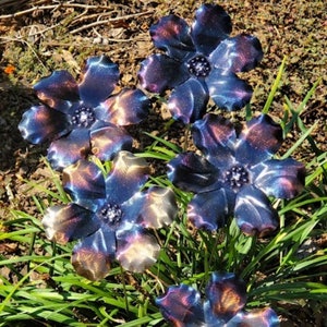 May include: Five metal flowers with iridescent blue, purple, and gold finishes. The flowers are arranged in a cluster and are set against a background of green grass.