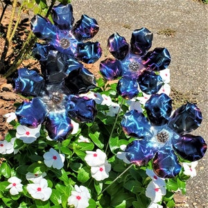May include: Four metal flowers with iridescent blue and purple coloring. The flowers are arranged in a cluster and are placed in a bed of white flowers.