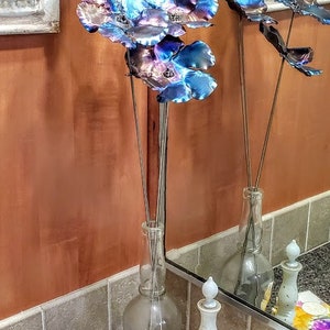 May include: A metal flower arrangement with blue and purple flowers in a clear glass vase. The flowers are on a black countertop with a white and yellow floral patterned soap bar.