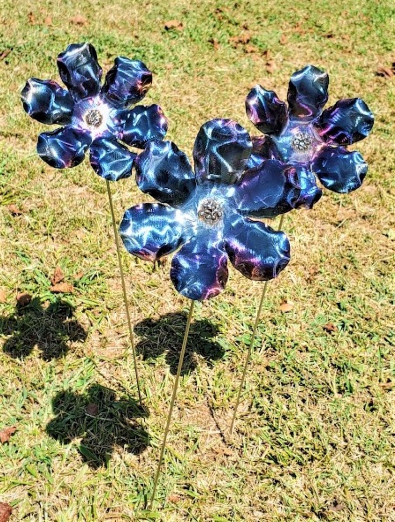 May include: Three metal flowers with blue and purple iridescent paint. The flowers are on thin metal stems and are arranged in a cluster.
