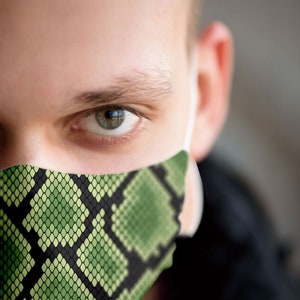 May include: A close-up of a person wearing a green and black snake skin patterned face mask. The mask covers the person's nose and mouth.