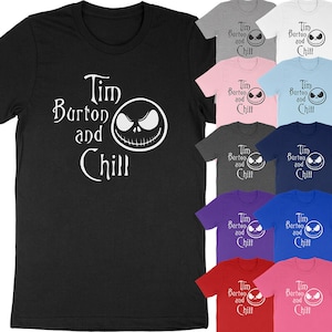 Op de afbeelding: Een zwart t-shirt met de witte tekst "Tim Burton and Chill" en een witte afbeelding van een gezicht. Extra t-shirts in verschillende kleuren, waaronder grijs, roze en blauw, zijn ook zichtbaar.