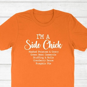 May include: Orange t-shirt with the text "I'M A Side Chick" in white script. Below the text are the words "Mashed Potatoes & Gravy, Green Bean Casserole, Stuffing & Rolls, Cranberry Sauce, Pumpkin Pie."
