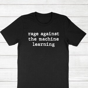 May include: Black t-shirt with the white text "rage against the machine learning". The shirt has short sleeves and a crew neck. The text is centered on the front of the shirt.