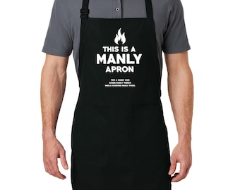 Puede incluir: Delantal negro con el texto blanco "THIS IS A MANLY APRON". El delantal tiene dos bolsillos delanteros y correas ajustables para el cuello y la cintura. Hay un gráfico de llama.